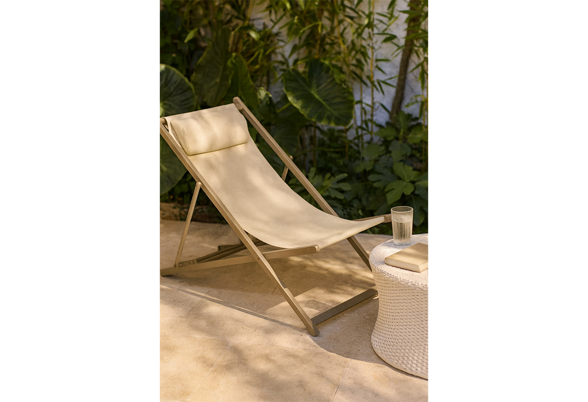 Απεικονίζεται η σεζλόνγκ σε κήπο δίπλα σε τραπέζι με νερό και βιβλίο πάνω του.